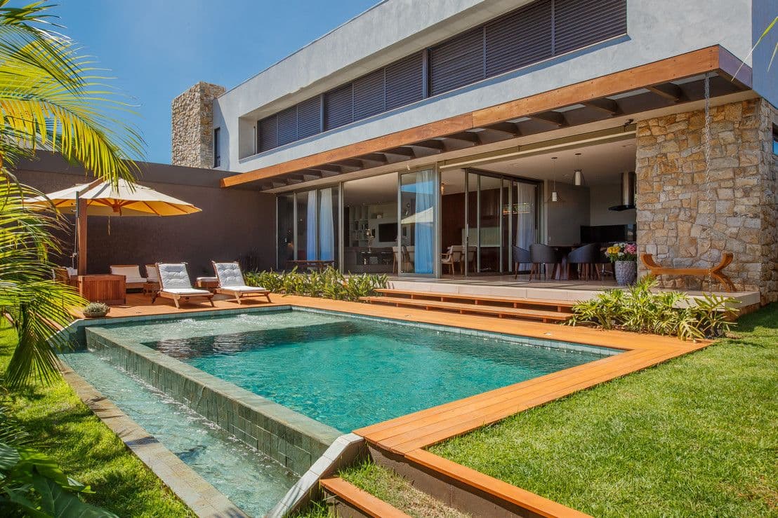 Casa moderna com piscina, deck de madeira, espreguiçadeiras e jardim em um dia ensolarado.